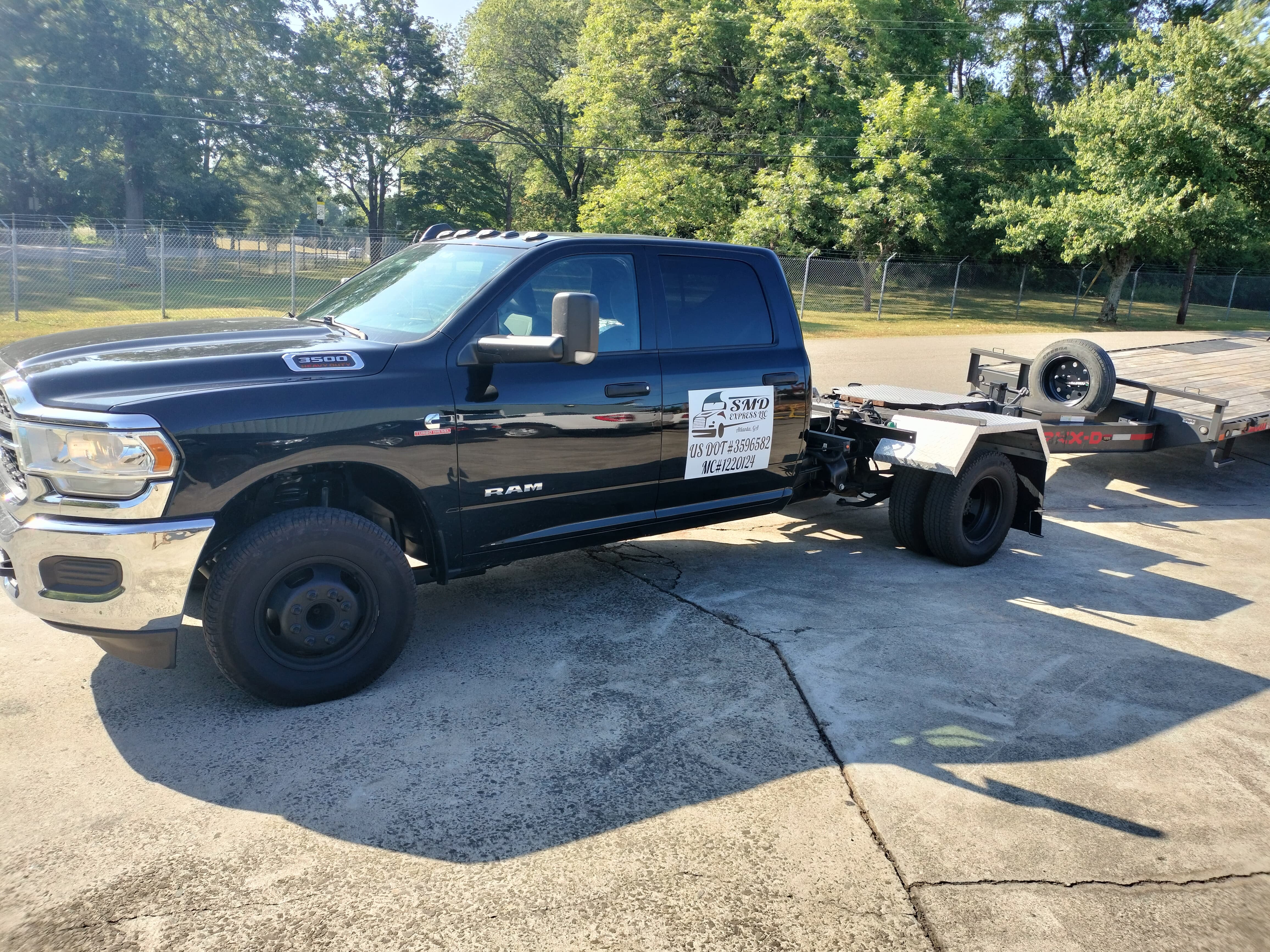 black Ram truck with a hotshot trailer attached to its back in the middle of a paved driveway with trees in the background